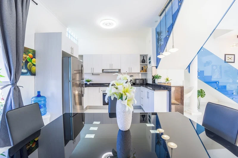 A modern kitchen with white cabinets, stainless steel appliances, and a dining area with a black table and chairs.