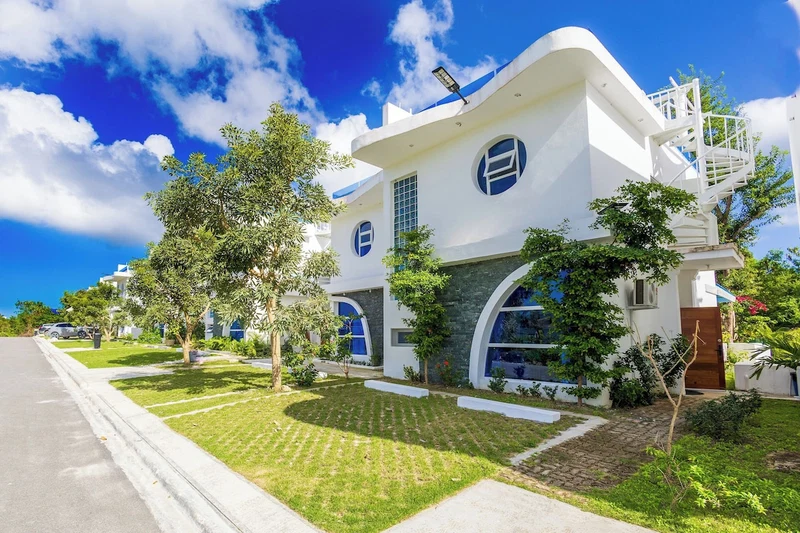 A modern white building with a curved facade, large windows, and a small garden area.