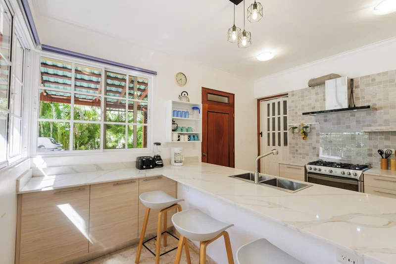 A modern kitchen with a large island, wooden cabinets, a built-in oven, and a window with a view of greenery.