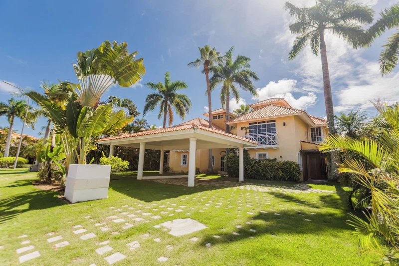 A house with a covered patio, palm trees, and a well-maintained lawn.