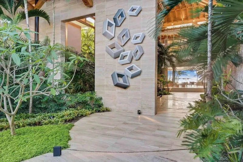 A modern building with a geometric wall design, surrounded by lush greenery and a paved walkway.