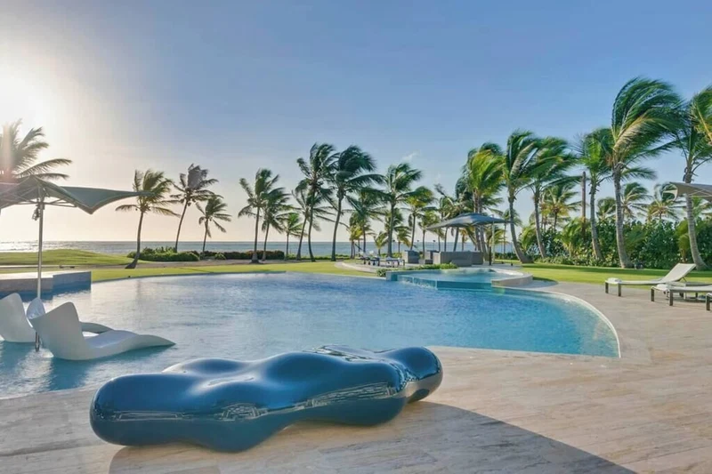 A pool area with a modern design, including a unique blue lounge chair and a clear view of the ocean.