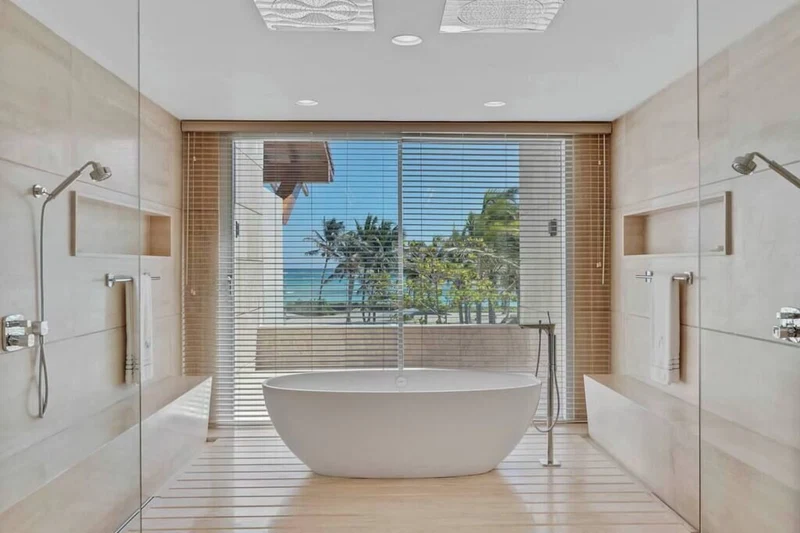 A modern bathroom with a freestanding bathtub, large windows, and a view of palm trees.