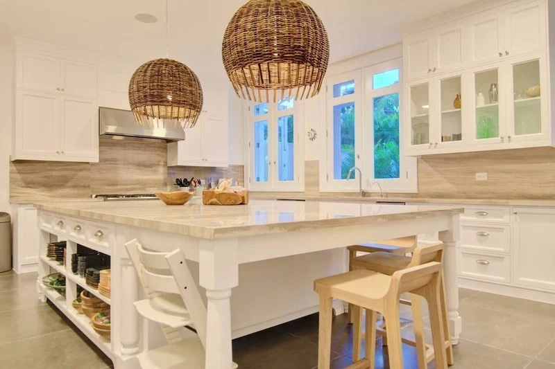 A spacious kitchen with a large island, white cabinetry, and two wicker pendant lights.