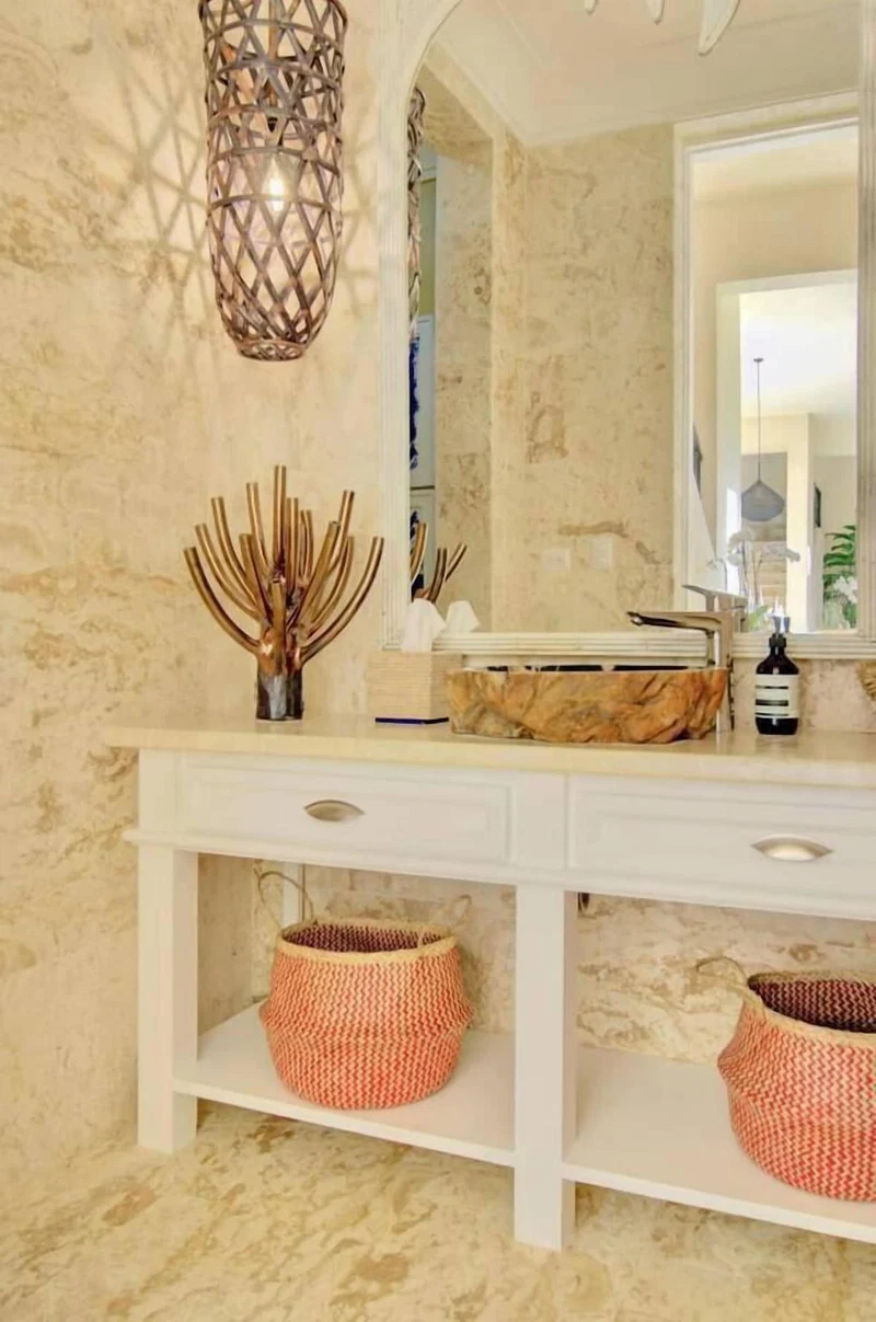 A bathroom with a marble wall, a white vanity, a mirror, a hanging light fixture, and two woven baskets on the vanity.