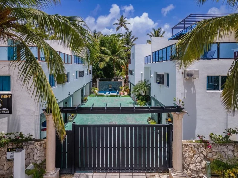 A gated resort with a pool, palm trees, and a clear blue sky.