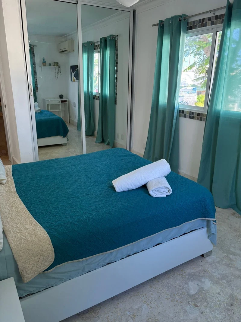 A bedroom with a bed, a mirror, and a window with curtains.