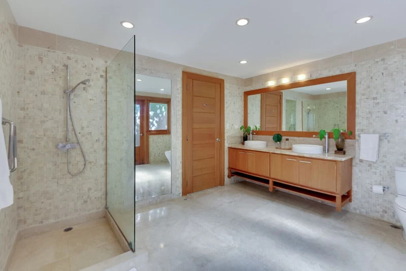 A modern bathroom with a glass shower enclosure, a wooden vanity with two sinks, and a large mirror above the vanity.