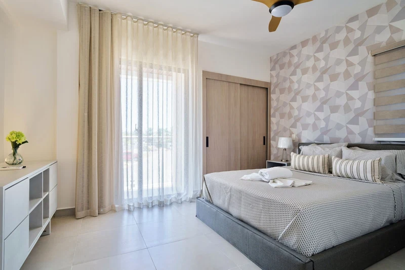 A modern bedroom with a bed, curtains, a nightstand, and a wall with geometric patterns.