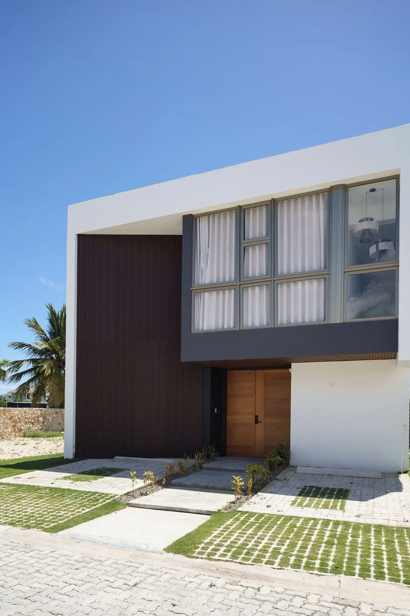 A modern two-story house with a large dark brown wall, a white facade, and a wooden door.