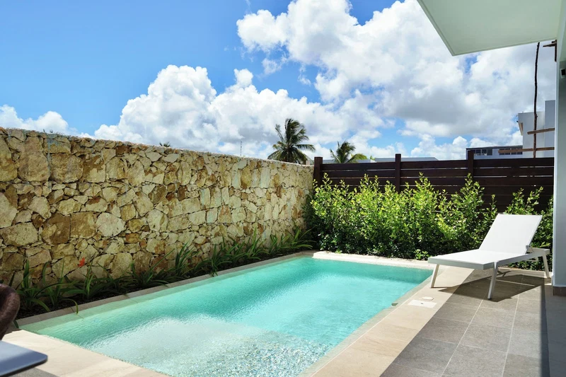 A swimming pool with a stone wall, a wooden fence, and a white lounge chair.