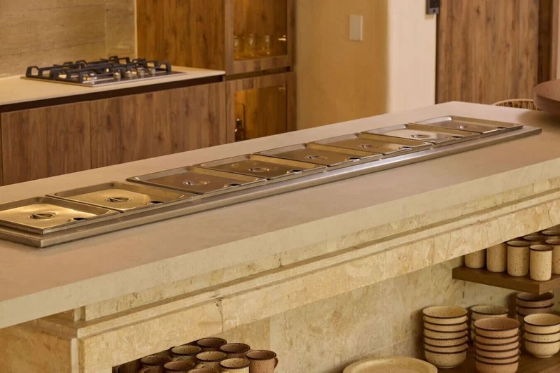A kitchen with a long countertop, a gas stove, and a variety of kitchenware including pots and pans.