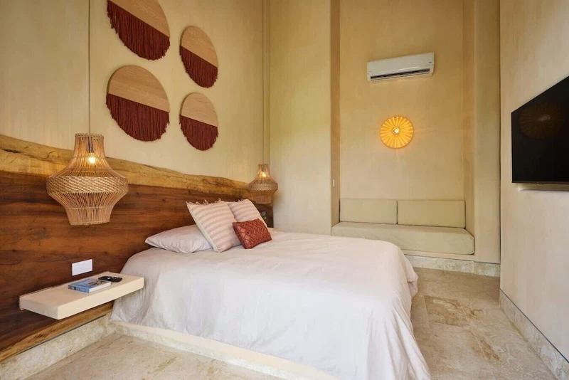 A bedroom with a wooden headboard, a bed with white bedding, two wall-mounted lamps, and a wall-mounted TV.