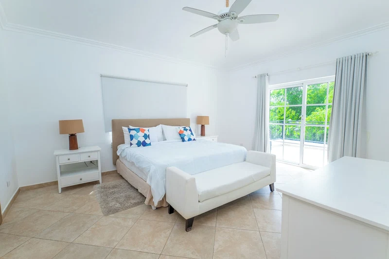 A bedroom with a bed, bedside tables, a ceiling fan, and a window with curtains.
