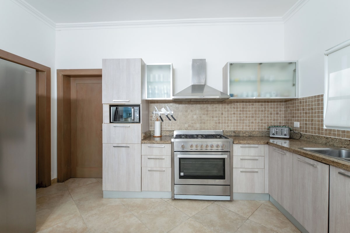 A modern kitchen with light wood cabinets, a stainless steel stove, and a microwave.