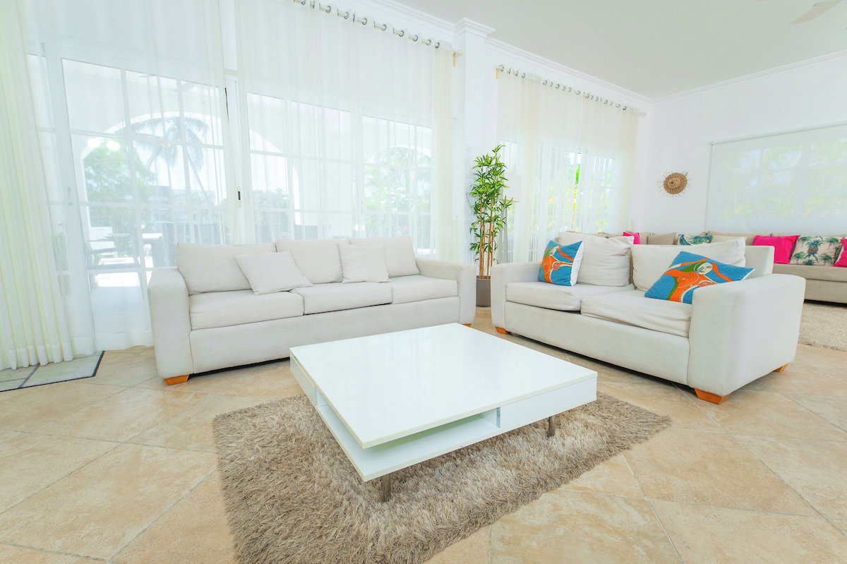 A modern living room with a white sofa, a coffee table, and a large window with curtains.
