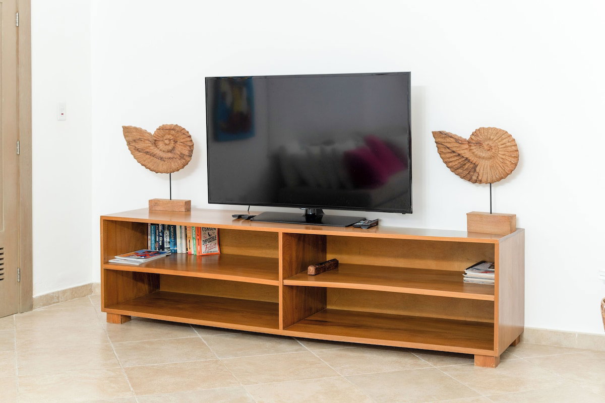 A wooden TV stand with a flat-screen TV, two decorative items on either side, and a shelf with books and magazines.