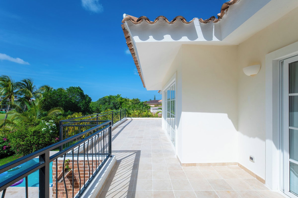 A balcony with a tiled floor, a metal railing, and a view of greenery and a distant building.