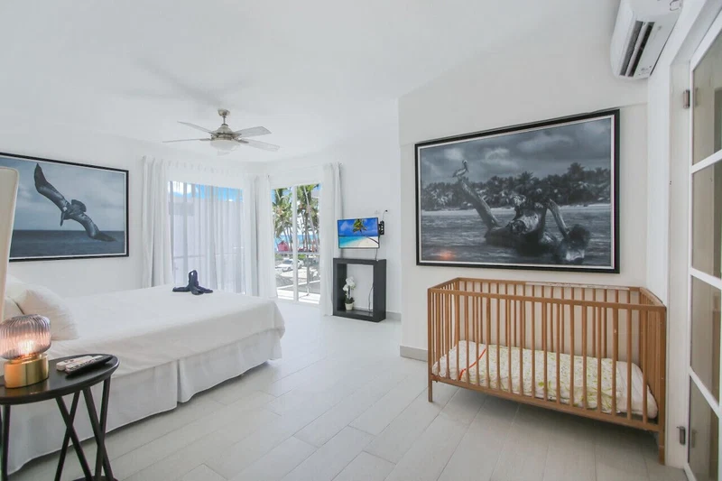 A bright, modern bedroom with a large bed, a crib, and artwork on the walls.