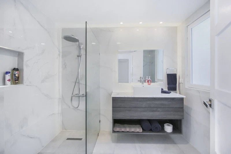 A modern bathroom with a glass-enclosed shower, a white sink, and a dark wood vanity.