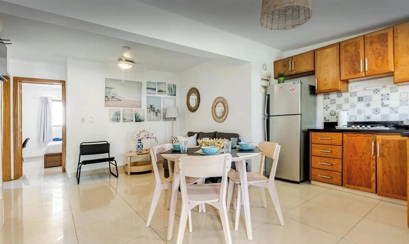 A modern kitchen with wooden cabinets, a refrigerator, and a dining area with a table and chairs.