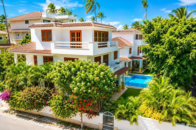 A multi-story building with a swimming pool, surrounded by lush greenery and palm trees.