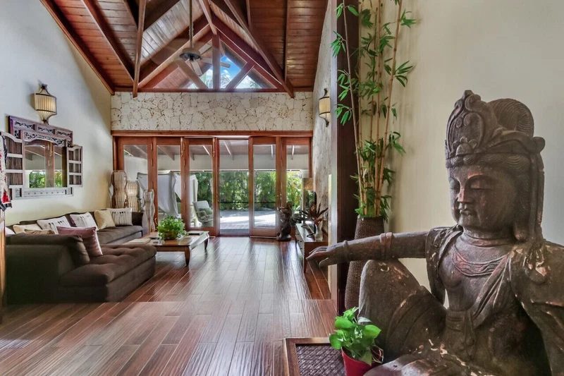 A spacious living area with a wooden ceiling, a large statue, and a view through glass doors to an outdoor space.