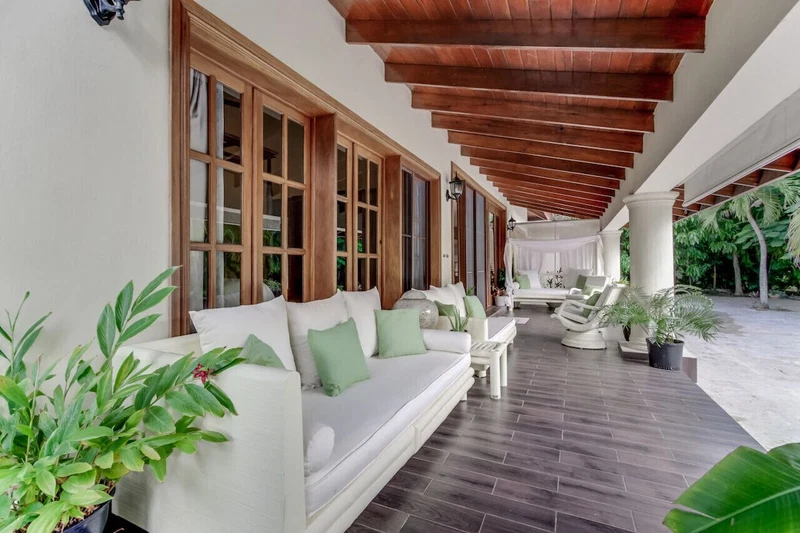 A covered outdoor seating area with a white sofa, green cushions, and potted plants.