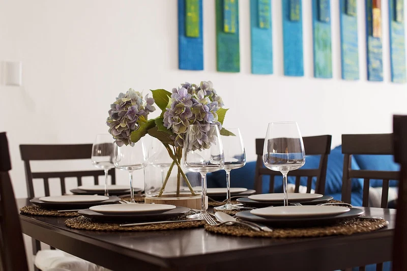 A dining table set with plates, cutlery, and wine glasses, with a vase of flowers in the center.