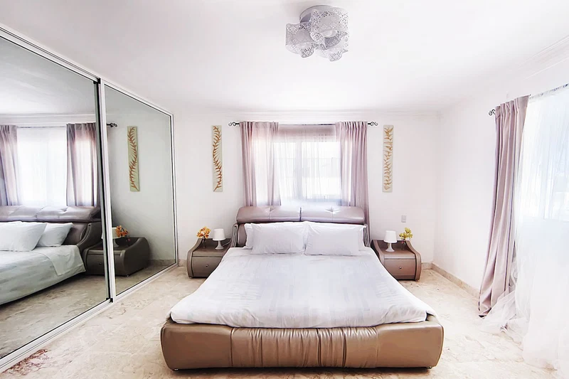 A modern bedroom with a large bed, a mirror, and a nightstand with a lamp.
