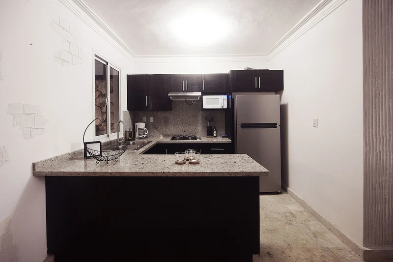 A compact kitchen with dark cabinets, a stainless steel refrigerator, and a granite countertop.
