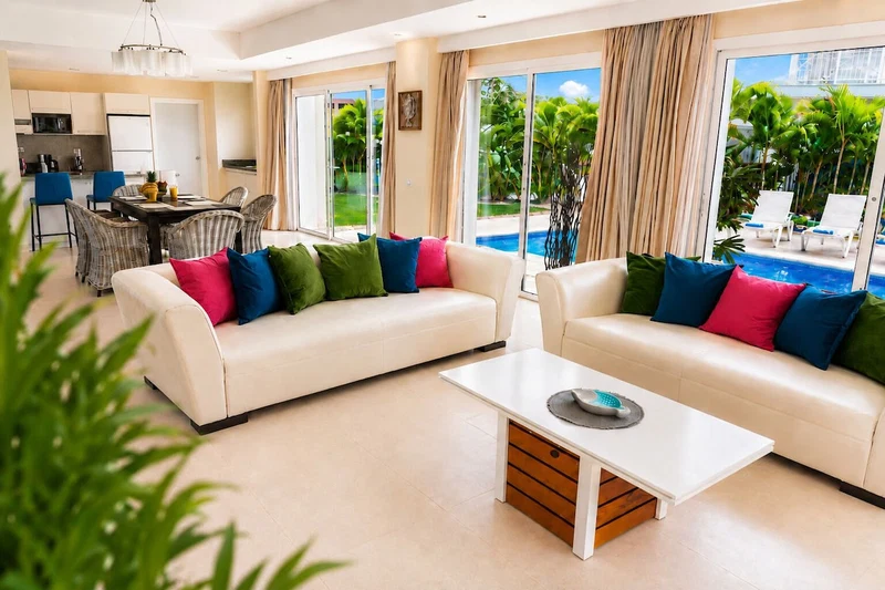 A modern living room with a sofa set, a coffee table, and a view of a pool and greenery.