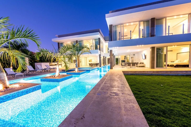 A modern two-story house with a swimming pool, lounge chairs, and a well-maintained lawn.