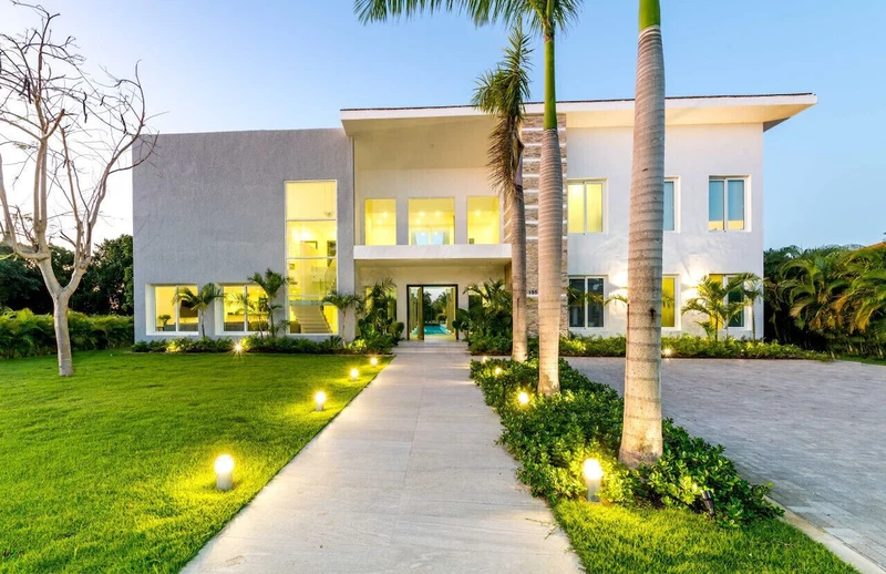 A modern two-story house with a well-maintained lawn, a pathway leading to the entrance, and several palm trees.