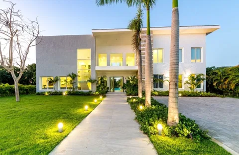A modern two-story house with a well-maintained lawn, a pathway leading to the entrance, and several palm trees.