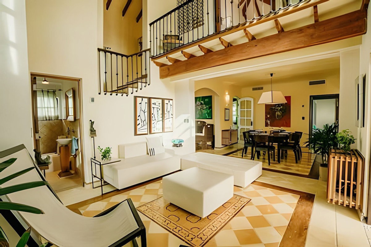 A spacious living area with a high ceiling, a staircase, and a dining area.