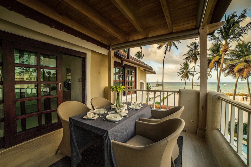 A dining area with a table set for four, overlooking a beach with palm trees and the ocean.