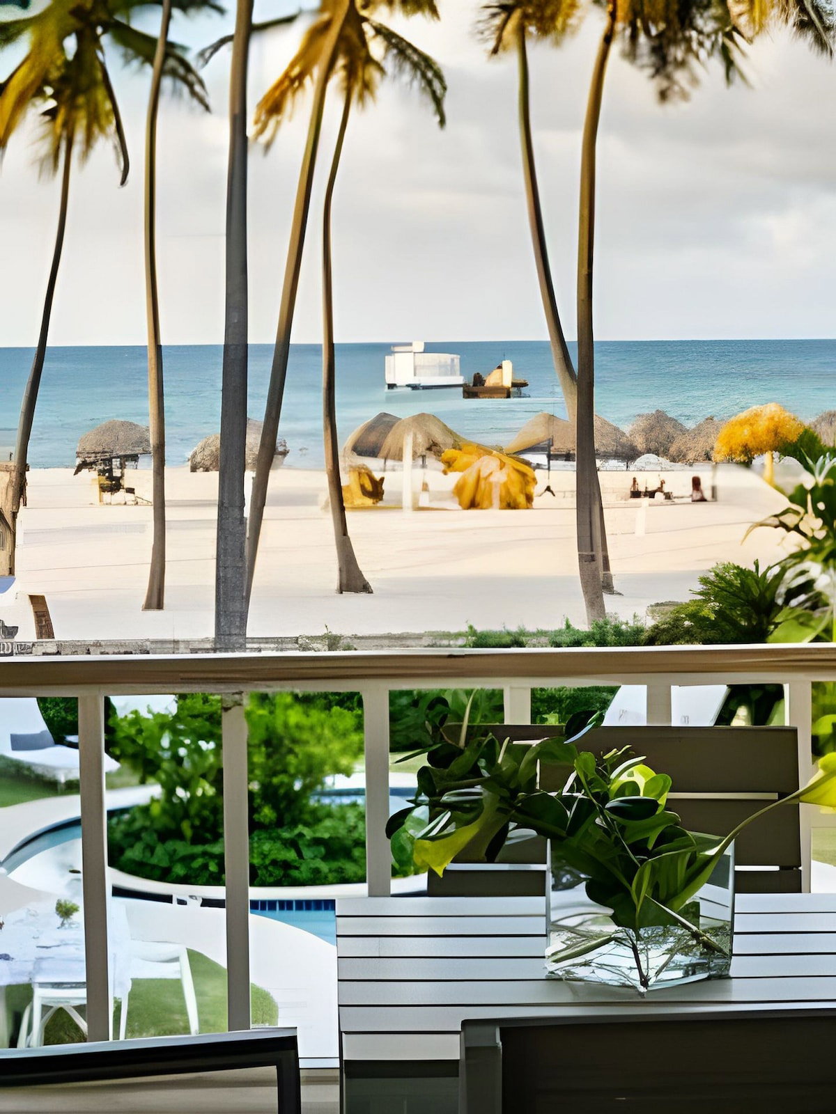 A beach view with palm trees, a white building, and a pool area.