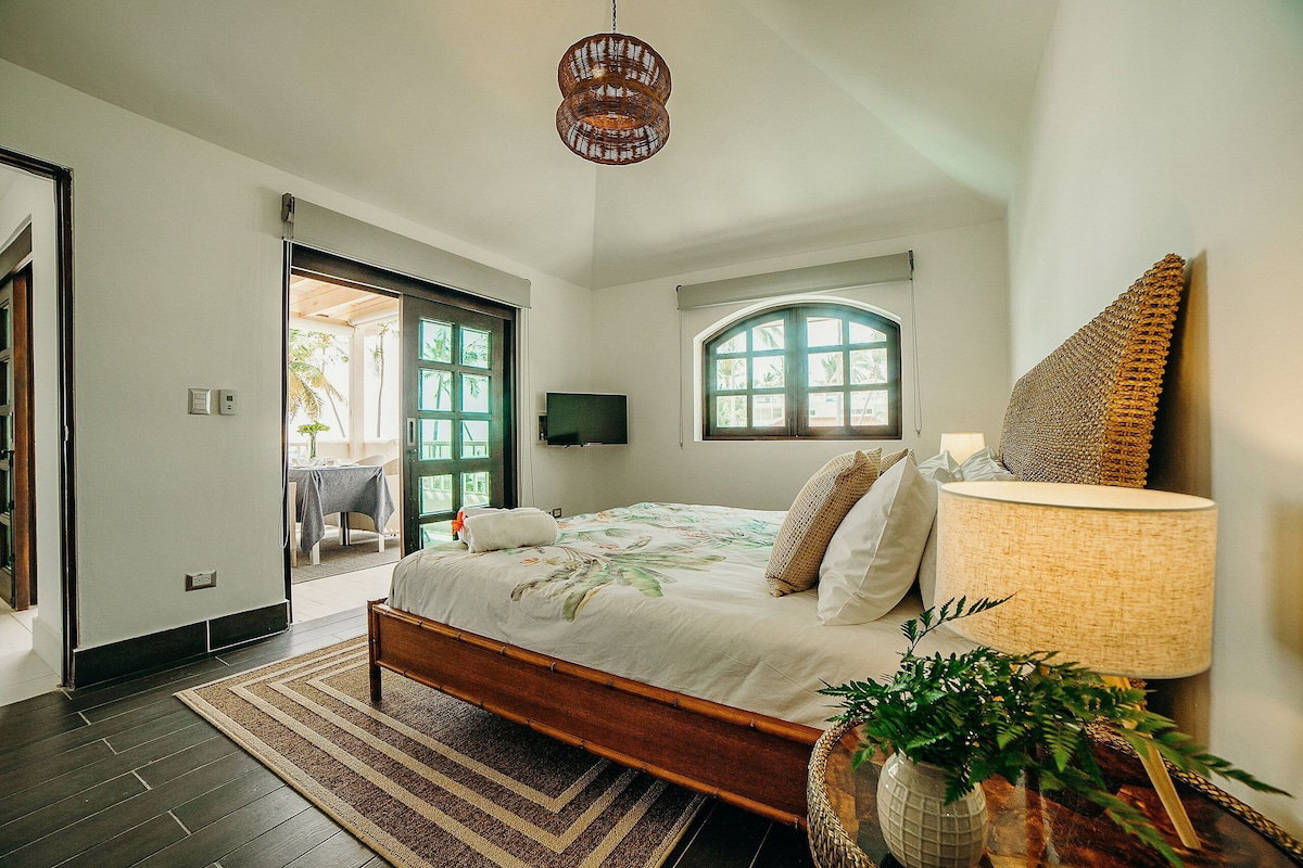 A bedroom with a bed, a bedside lamp, a TV, and a view of the outdoors.