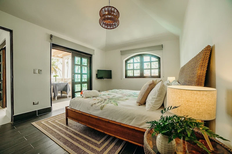 A bedroom with a bed, a bedside lamp, a TV, and a view of the outdoors.