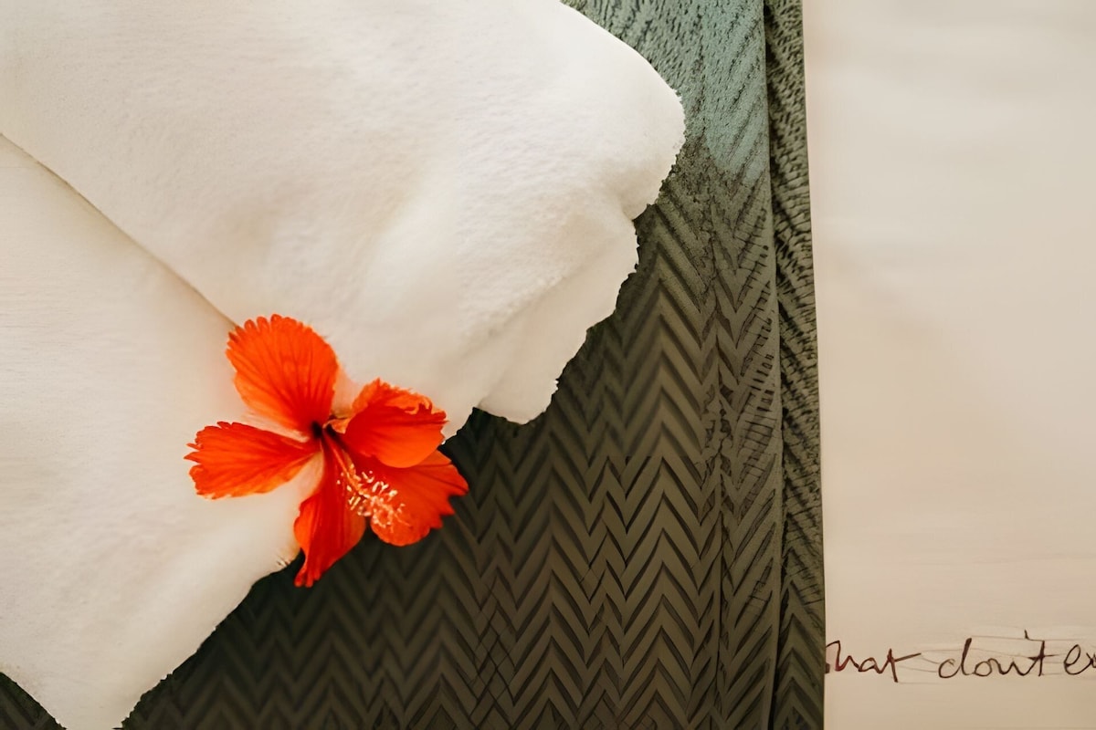 A white towel with a hibiscus flower on a textured green pillow.
