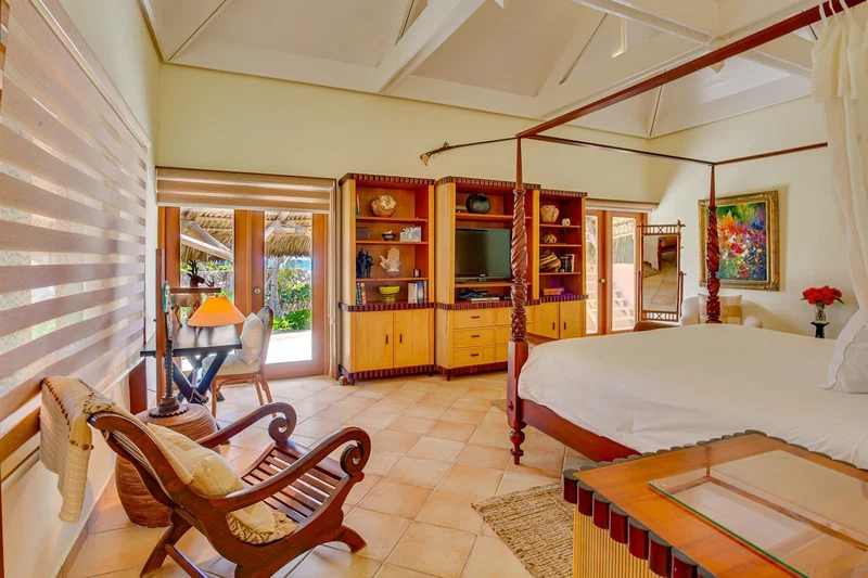 A spacious bedroom with a four-poster bed, wooden furniture, and a large window offering a view of the outdoors.