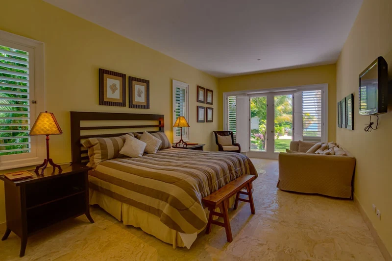 A bedroom with a bed, bedside tables, a bench, a chair, and a television.