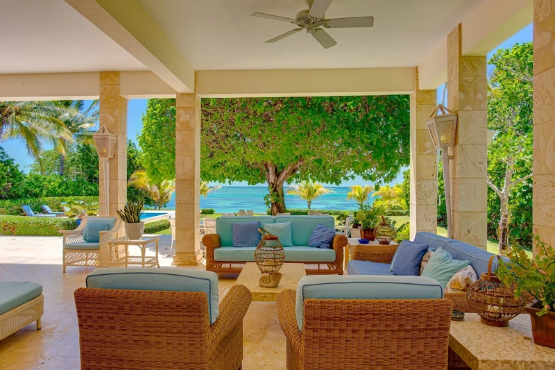 A covered outdoor seating area with wicker furniture, a ceiling fan, and a view of the ocean.