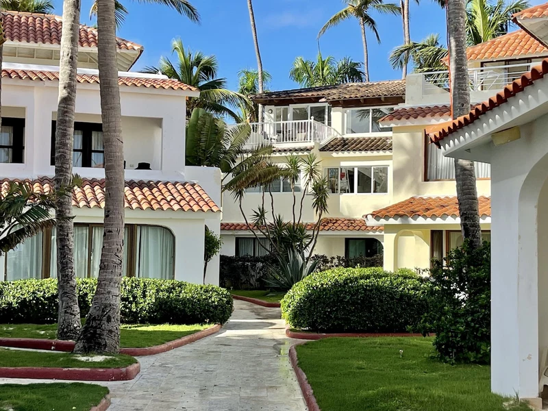 A resort with multiple-story buildings, palm trees, and a central pathway.