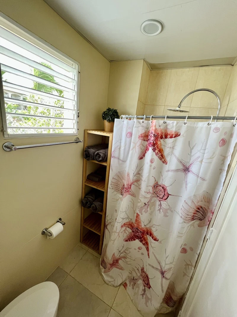 A bathroom with a shower curtain featuring a floral pattern, a toilet, a towel rack, a shelf with folded towels, and a window with blinds.