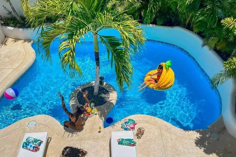 A swimming pool with palm trees, lounge chairs, and a person in a yellow float.